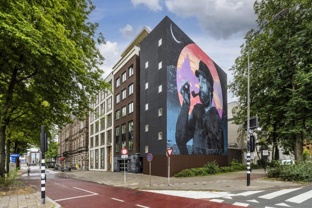 Muurschildering van een man met een pijp op een gebouw aan de Prins Hendrikkade in Amsterdam.